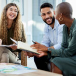 Tres personas sonrientes colaborando en una reunión, ejemplo de impacto social de una empresa y trabajo en equipo en el marco de Mediolanum Aproxima